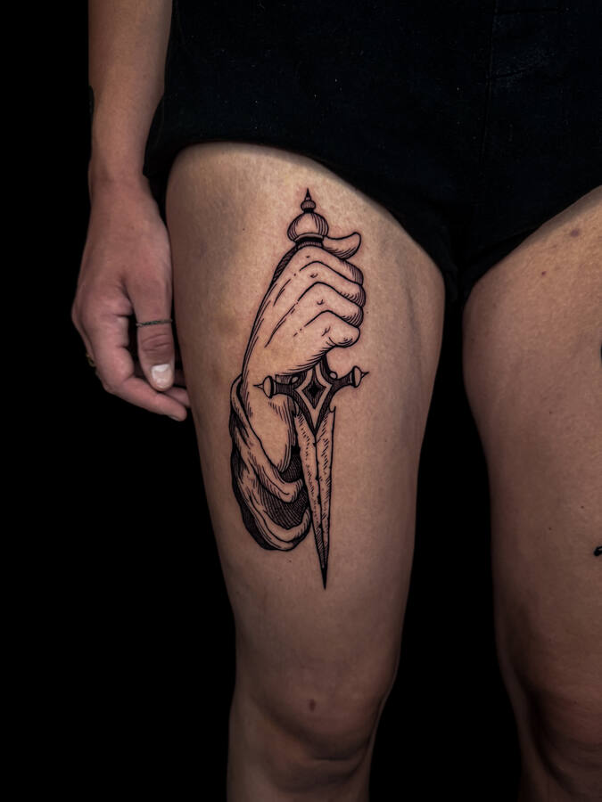 Main tenant une dague, tatouée sur une cuisse